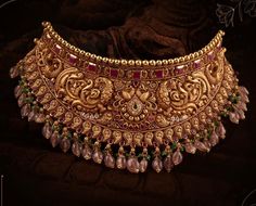 an elaborate gold necklace with pearls and garnets on the neck, set against a dark background