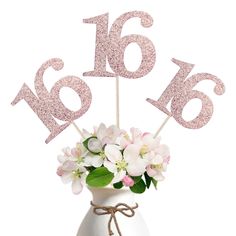 a white vase filled with pink flowers and numbers on top of each number is 16