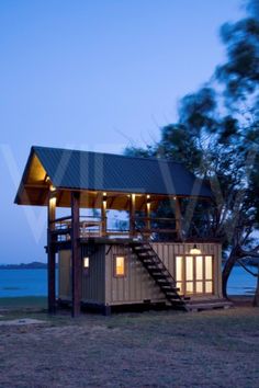 a house made out of shipping containers sitting on top of a field next to the ocean