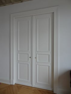 an empty room with two white doors and hard wood flooring