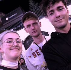 three people standing next to each other in front of a building and one person wearing glasses