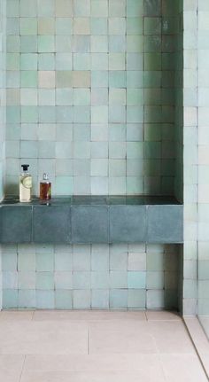 a bathroom with blue tiles and a shelf in the corner that holds two soaps