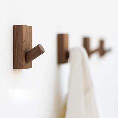 two wooden hooks mounted to the side of a white wall next to a towel rack