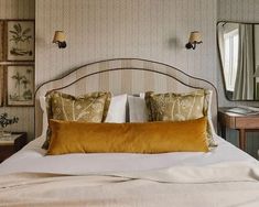 a bed with two pillows on top of it next to a night stand and mirror