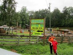 a man and woman standing in front of a sign for a petting zoo on the side of a road