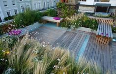 a wooden deck surrounded by tall grass and flowers in front of a large white building