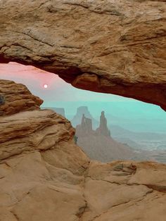 the sun is setting through an opening in a rock formation