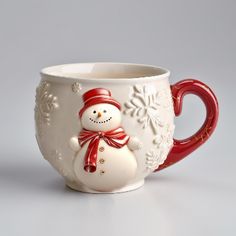 a white cup with a red handle and a snowman design on the side, sitting in front of a gray background