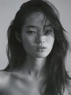 black and white photograph of a woman with long hair looking at the camera while wearing a bra