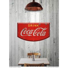 a coca cola sign hanging from the side of a wooden wall next to a table