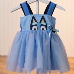 Blue dog character dress with a tulle overlay skirt and a double ribbon bow on the side. This dress features a sweet character dog embroidery design with her peeking up from the bodice.  The shoulder straps allow for ease of dressing, and the back of the bodice has encased elastic that will stretch allowing for longer wear. This dress can be layered with a shirt underneath for cooler weather or wear as a sundress for warmer days. Would be a cute dress to wear at a themed birthday party or even as a flower girl at a wedding.  All of my dresses and outfits are hand made by myself one at a time in my small studio. I try to source American made supplies whenever available.  Sizes are from 9-12 months to 5T. This item ships within 2 weeks. I do have a few sizes pre-made so they will ship the ne Double Ribbon Bow, Dog Party Dress, Tulle Overlay Skirt, Dog Character, Dog Embroidery Designs, Blue Tutu, Bluey Birthday, Dog Embroidery, Sisters Dress