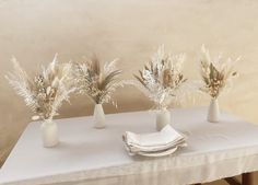 three white vases with dried plants in them on a table cloth covered tablecloth