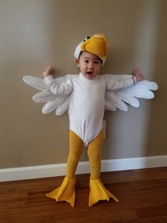 a baby dressed in a chicken costume standing on the floor with his arms spread out