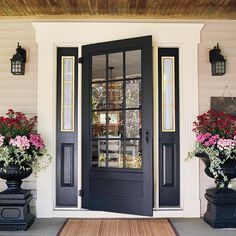 the front door is painted black and has flowers in large urns on either side