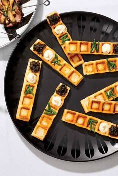 several waffles are arranged on a black plate with green garnishes