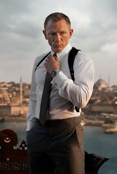 a man wearing a white shirt and black tie standing in front of a body of water