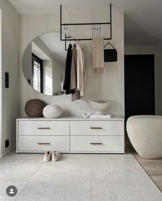 a white dresser sitting under a mirror next to a wall mounted coat rack with clothes hanging on it