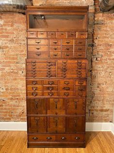 an old wooden cabinet with many drawers on it in front of a red brick wall