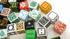 many different colored dices sitting on top of a white table together, all with black and green designs