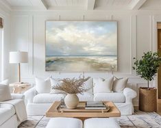 a living room filled with white furniture and a painting on the wall above it's coffee table