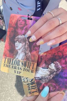 a person holding up two tickets with their hands and nails painted blue, pink, yellow and purple