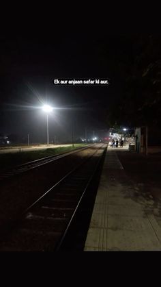 an empty train track at night with people walking on the platform and lights in the background