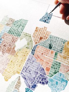 a person is drawing a map with watercolors on white paper and has a pen in their hand