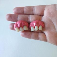 a hand holding two pink and white tooth shaped objects in it's palm area