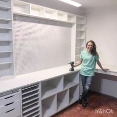 a woman standing in front of a white wall with shelving and drawers on it