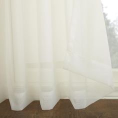 a white curtain hanging on the side of a window in front of a wooden floor