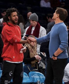 two men shaking hands while standing next to each other in front of an audience at a basketball game