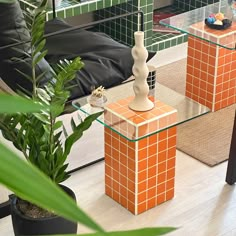 an orange and white vase sitting on top of a glass table next to a plant