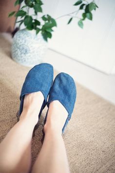 a woman's feet in blue slippers on the floor next to a potted plant