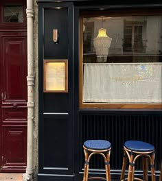 two stools sitting in front of a storefront with a sign on the window