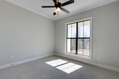 an empty room with a ceiling fan and large window in the corner, all white