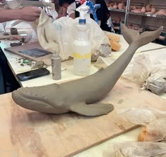 a clay whale sitting on top of a wooden table next to plastic bags and bottles