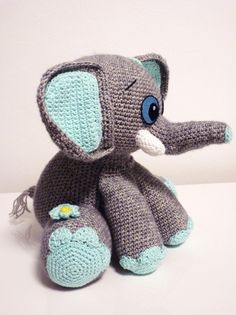 a crocheted stuffed elephant with blue eyes sitting on a white surface, it's made to look like an elephant