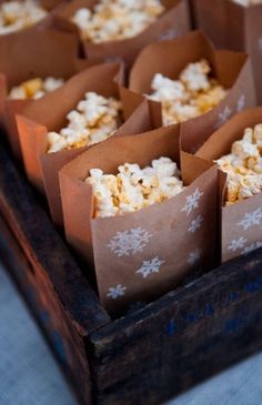 small brown paper bags filled with popcorn on top of a wooden tray covered in snowflakes