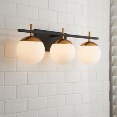 three white and gold lights hanging from a black metal fixture on a wall in a bathroom