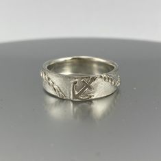 a silver ring with an anchor and rope design on the side, sitting on a table