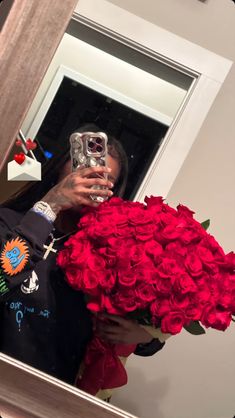 a woman taking a selfie in front of a mirror holding a bouquet of red roses