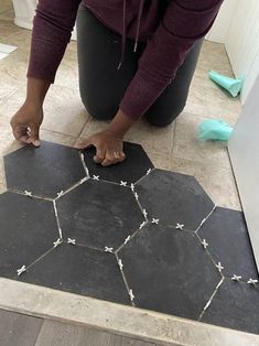 a person kneeling down on the floor with their hand on top of a piece of black tile