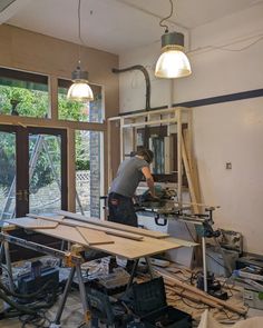 a man is working on some wood in a room with windows and other items around him