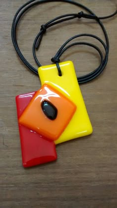 a yellow and red square shaped pendant on a black cord