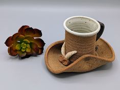 a brown cowboy hat next to a flower on a gray surface with a white vase in the background