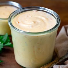 two jars filled with food sitting on top of a wooden table next to parsley