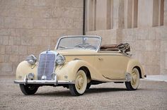 an old yellow car parked in front of a stone building with a brown leather seat