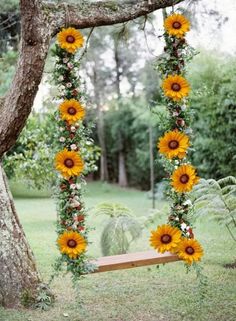 a wooden swing with sunflowers and greenery hanging from it's sides