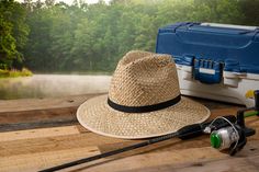 a hat, fishing rod and reel sitting on a wooden table next to a cooler