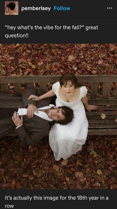 a man and woman laying on top of a wooden bench covered in leaves next to each other